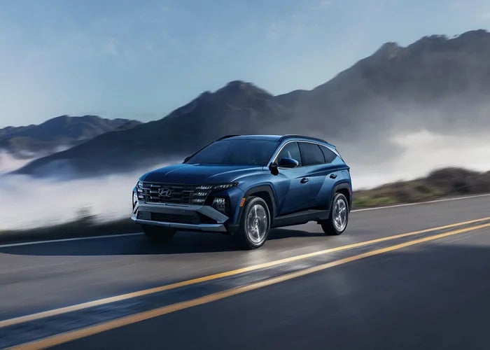 A dark blue 2026 Hyundai Tucson Hybrid SUV driving down a misty mountain road