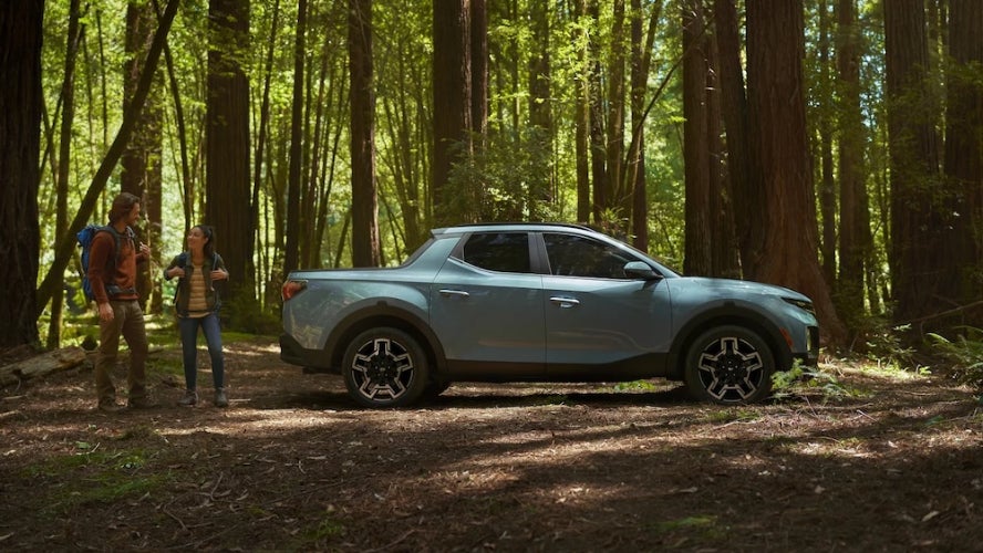 Two hikers walking towards a light blue 2026 Hyundai Santa Cruz parked in the woods