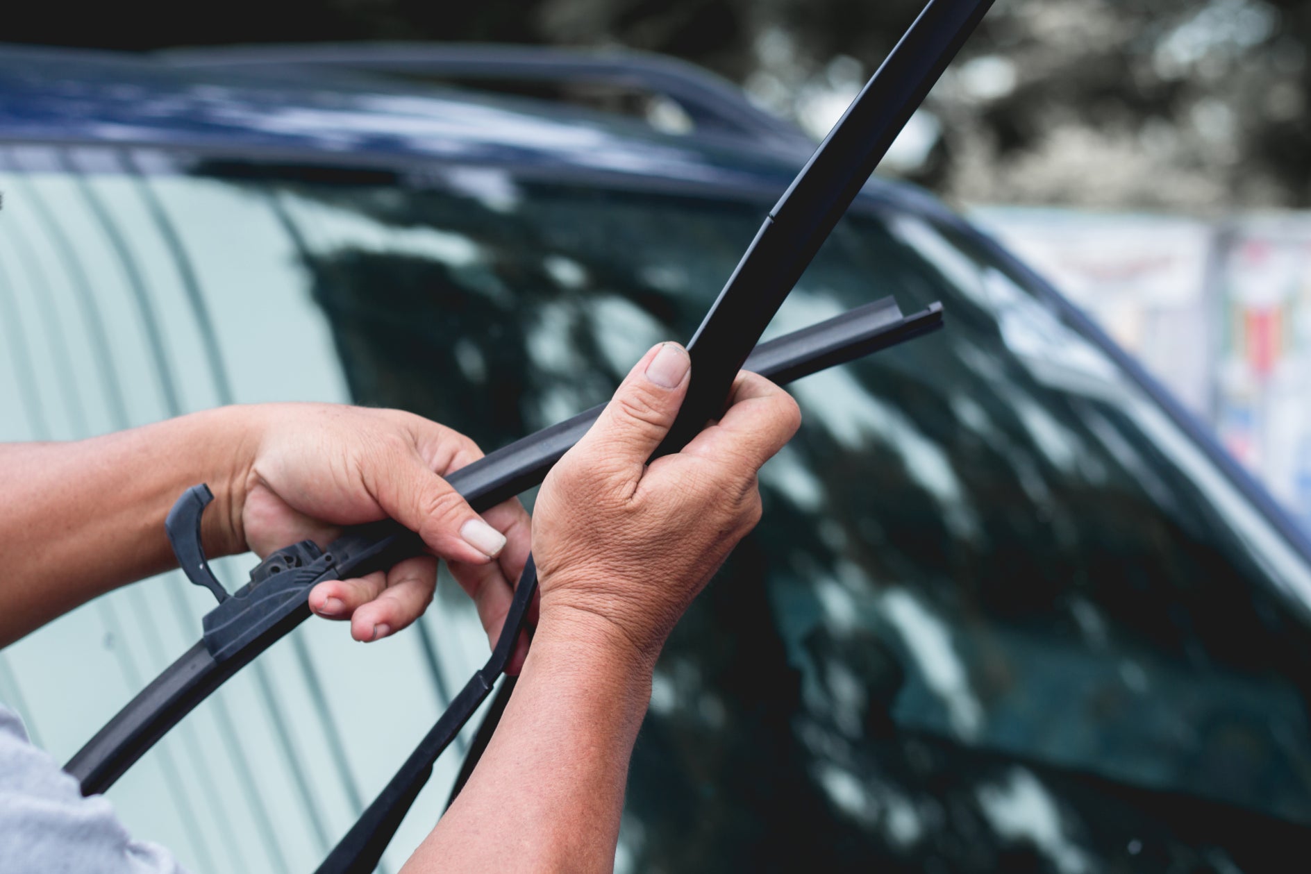 The hands of a light-skinned person replacing the windshield wiper blades of a vehicle