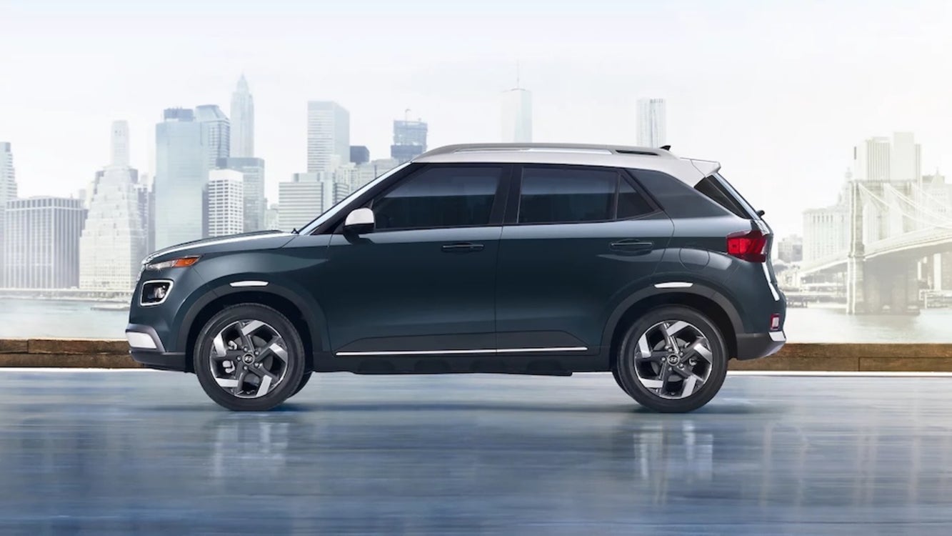 A gray 2026 Hyundai Venue SUV parked near a river with a city in the distance