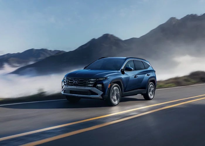 A dark blue 2026 Hyundai Tucson SUV driving down a misty mountain road