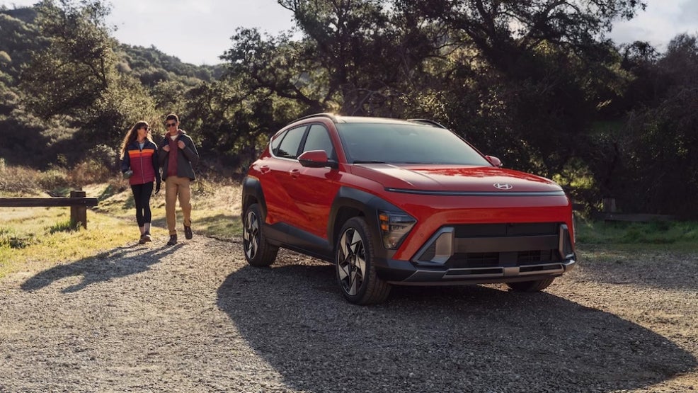 Two hikers walking toward a red Hyundai Kona SUV parked at a trailhead