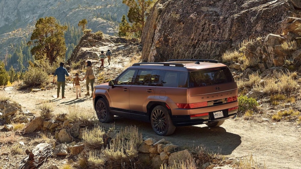 A family walking away from a copper 2026 Hyundai Santa Fe SUV parked on a mountain path