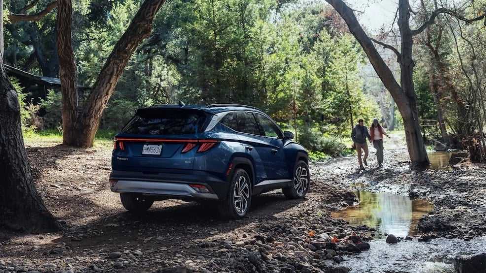 A dark blue 2025 Hyundai Tucson SUV parked on a muddy road, with two hikers walking nearby