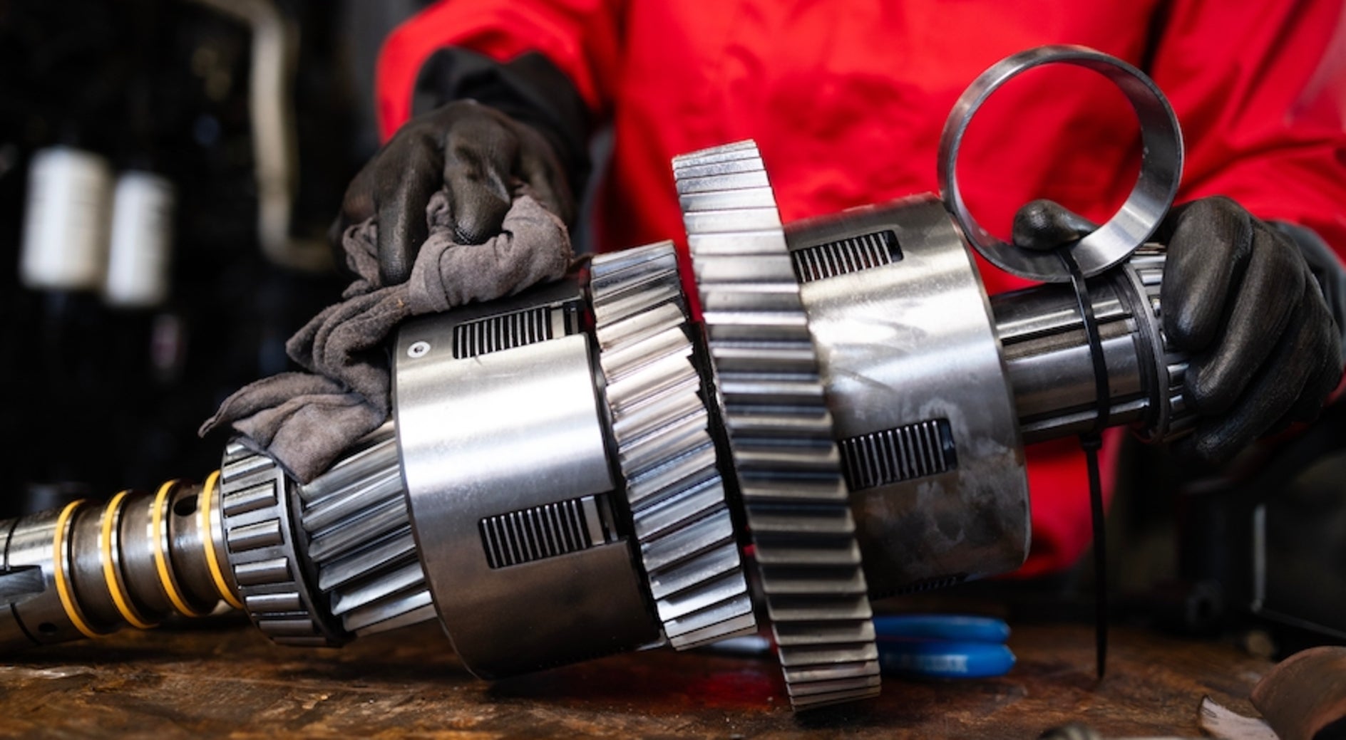 A person in black gloves and red coveralls polishing the transmission of a vehicle with a rag