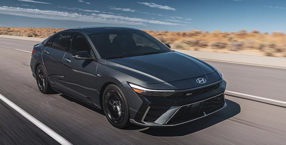 A dark gray 2025 Hyundai Elantra sedan driving down a desert road