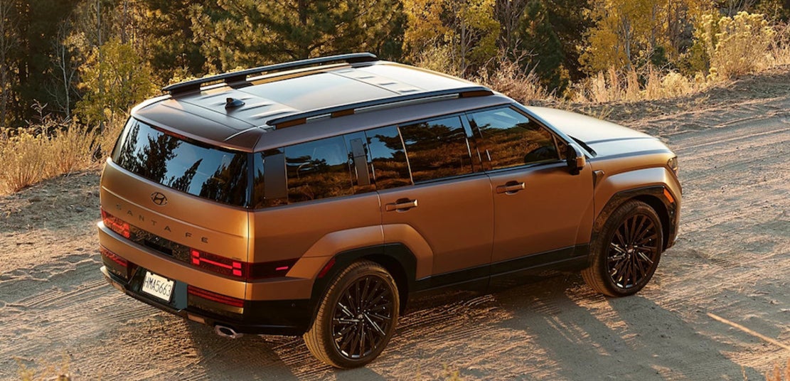 An orange 2025 Hyundai Santa Fe SUV driving along a dirt road