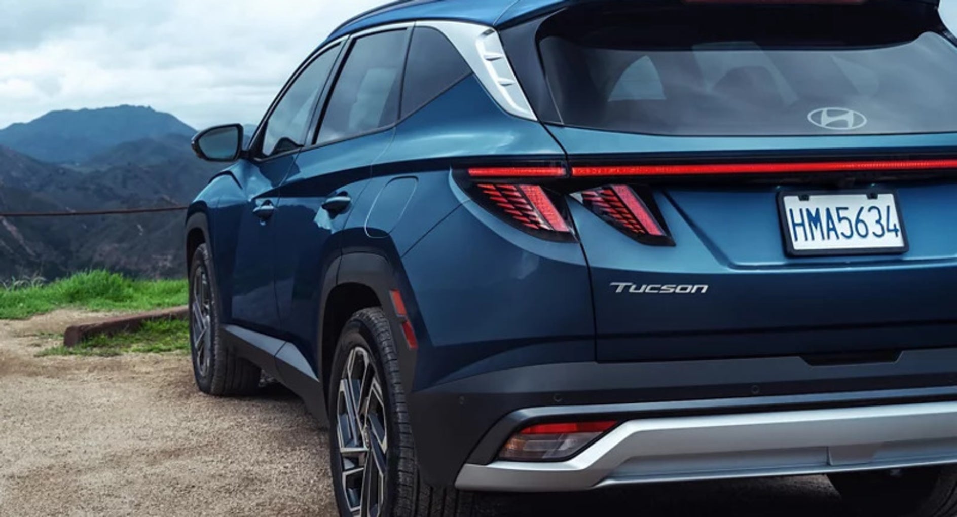 A three-quarters view of the back of a dark blue 2025 Hyundai Tucson SUV parked on the edge of a mountain ledge
