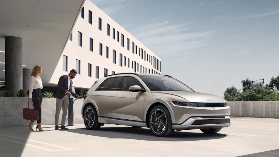 Two people charging a beige 2026 Hyundai Ioniq 5 SUV