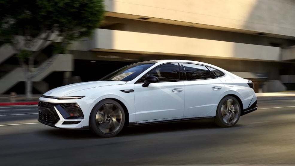A side view of a white 2026 Hyundai Sonata sedan driving down a city street
